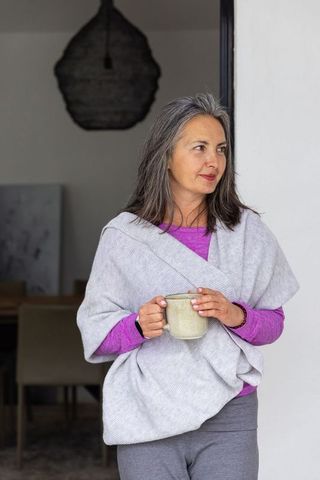 Mature woman standing in doorway holding ceramic mug, enjoying quiet morning at home