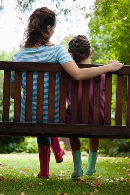 Rear view of girl and woman sitting on wooden bench at backyard