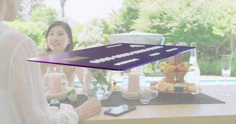 Floating purple credit card hovering over poolside dessert table, multigenerational gathering