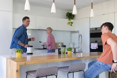 Family cooking together in modern bright kitchen with wooden island and fresh herbs