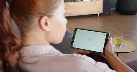Woman relaxing on sofa holding tablet with calibration targets and cup of tea