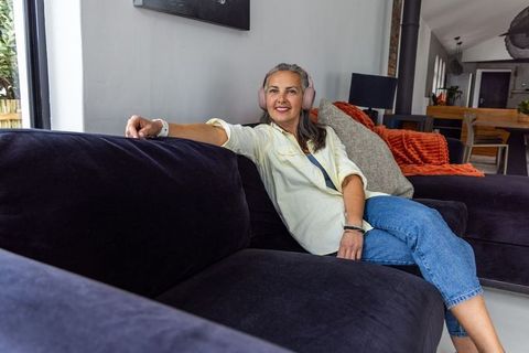 Senior woman relaxing on velvet sectional wearing pink headphones and smiling in living room