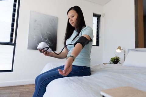 Mature asian woman measuring blood pressure at home using digital arm cuff and monitor