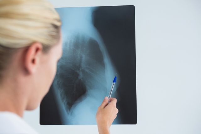 Cropped image of female doctor examining X-ray against gray background