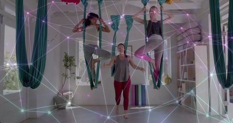 Women practicing aerial yoga in teal hammocks, group fitness training in bright studio