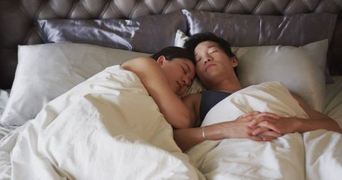 Couple cuddling under white duvet on tufted headboard bed, intimate morning resting