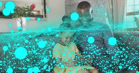 Father and daughter sitting on sofa with turquoise particle overlay, cozy family moment