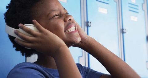 African student smiling while listening to music on white headphones in school hallway