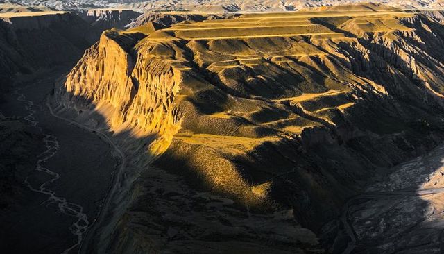 Sunlit plateau revealing layered cliffs and braided river in deep canyon