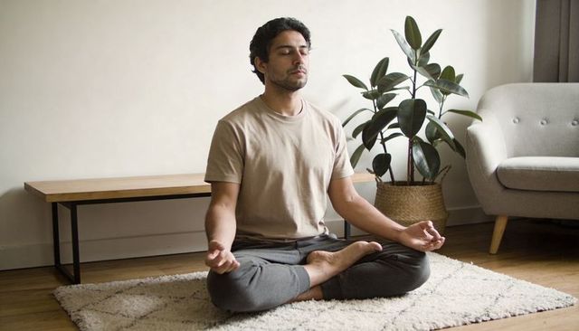 Young man meditating cross-legged on shag rug in minimalist living room with houseplant