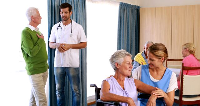 Depicts elderly care facility with healthcare professionals interacting with senior citizens. Nurse comforting woman in wheelchair while doctor converses with male resident in background. Suitable for articles, brochures, and promotional material on elderly care, nursing homes, and healthcare facilities.