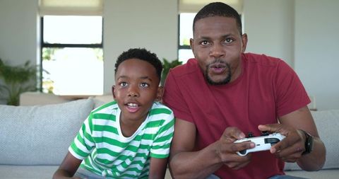 African american father and son playing video games on sofa, bonding through gaming