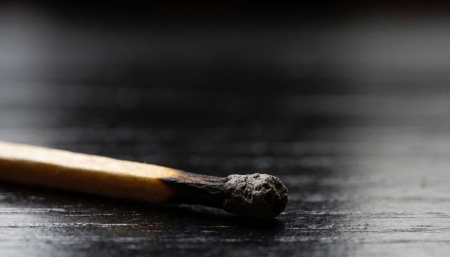 Burned matchstick with ash on dark wood macro still life with shallow bokeh