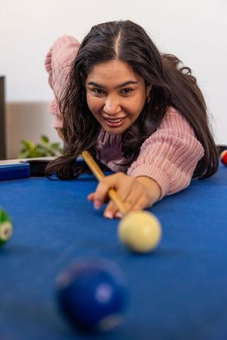 Asian woman leaning over blue pool table aiming cue with focused smile
