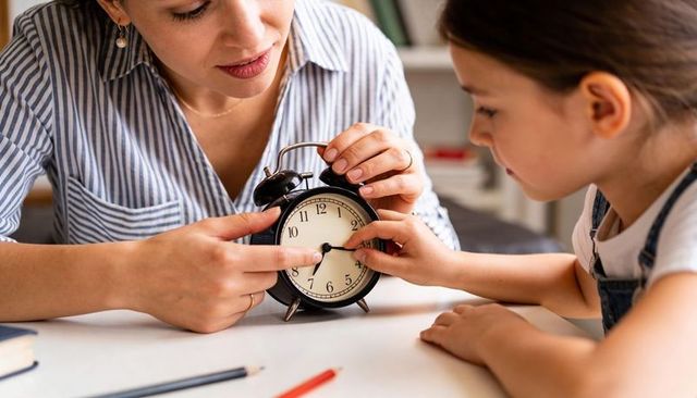 Mother guiding child learning to tell time with vintage alarm clock at home