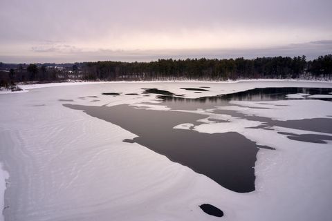 Aerial view of frozen lake with dark open water and snow patterns under overcast sky