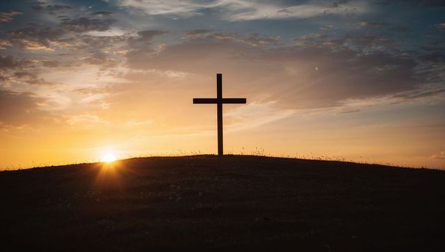 Solitary cross silhouetting on hilltop during golden sunset
