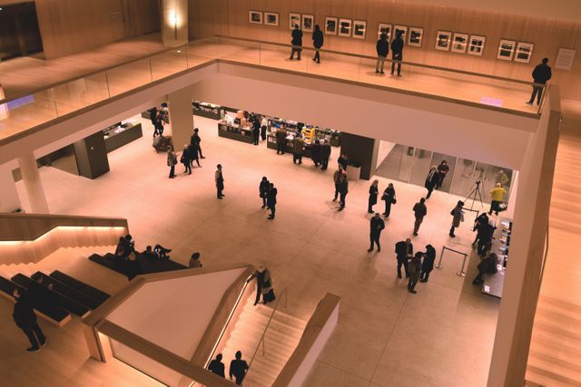 Depicts visitors exploring a spacious modern art gallery. The open layout with mezzanine and staircase provides ample room for guests. Useful for themes related to art appreciation, culture, interior design of public spaces, and educational content.