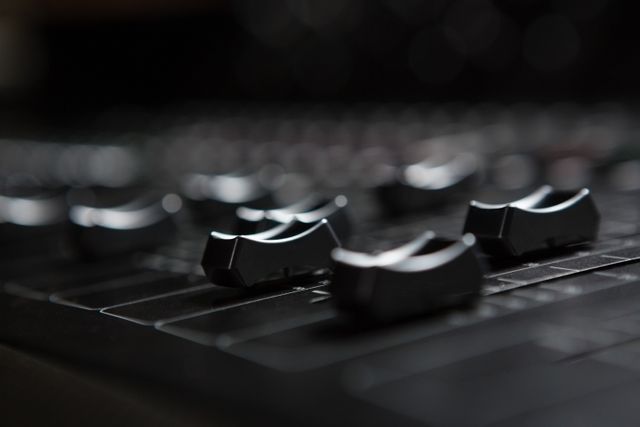 This close-up of sound mixer sliders in a recording studio is perfect for use in music production articles, sound engineering tutorials, audio equipment reviews, and advertisements for recording studios. It illustrates the professional environment and tools used in sound mixing and music production.
