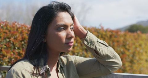 Mid adult indian woman sitting on park bench contemplating autumn sunlight serene portrait