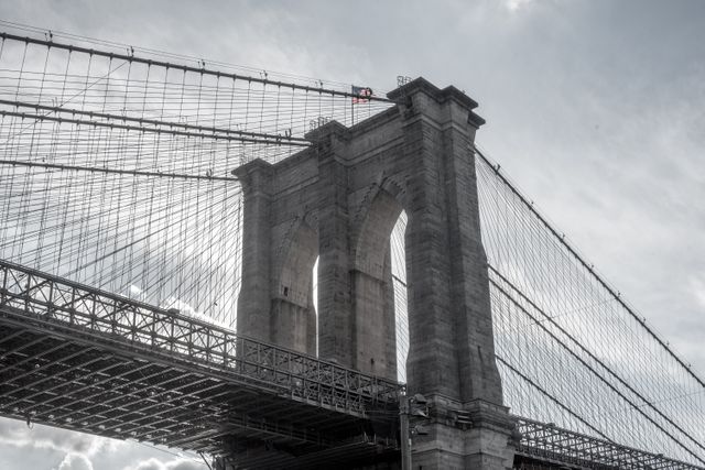 Depicts close view of Brooklyn Bridge showcasing its detailed architecture under a dramatic sky. Brooklyn Bridge's intricate cables and towers highlight creative urban infrastructure. Ideal for travel enthusiasts, engineering lovers, and marketers looking to emphasize iconic New York landmarks. Suitable for use in blogs, educational materials, presentations, and travel documentaries.