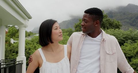 Interracial Couple Embracing Under Overcast Sky Surrounded by Verdant Greenery