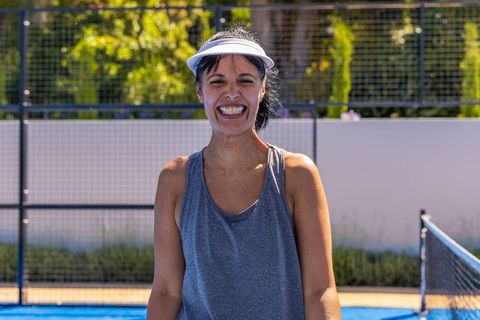 African american mature woman smiling on blue tennis court wearing visor and tank top