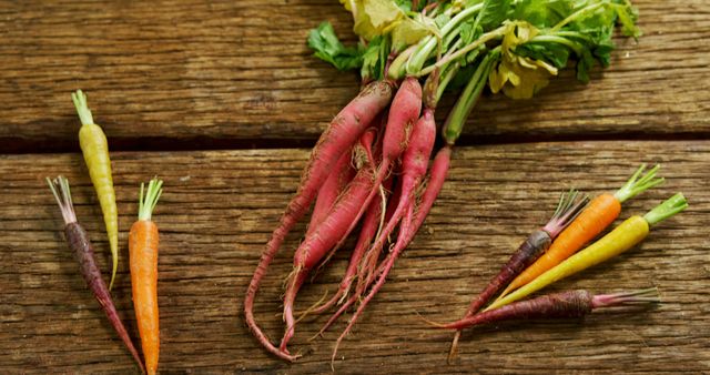 Colorful carrots with green tops are laid out on a rustic wooden surface, showcasing a variety of colors from orange to purple. These vibrant root vegetables highlight the natural diversity found in healthy, farm-fresh produce.