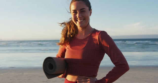 Portrait of caucasian woman holding yoga mat at the beach smiling. healthy active lifestyle, outdoor fitness and wellbeing.