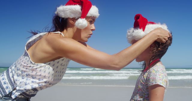 Mother Adjusting Daughter's Santa Hat on Sunny Beach - Download Free Stock Images Pikwizard.com