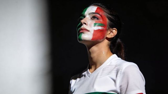 Gazing female athlete with italian tricolor face paint in locker-room spotlight
