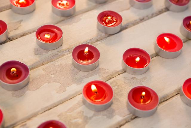 Red tealight candles burning on a wooden plank create a warm and cozy atmosphere, perfect for holiday decor, Christmas celebrations, or spiritual practices. Ideal for use in festive greeting cards, home decor inspiration, or relaxation and meditation themes.