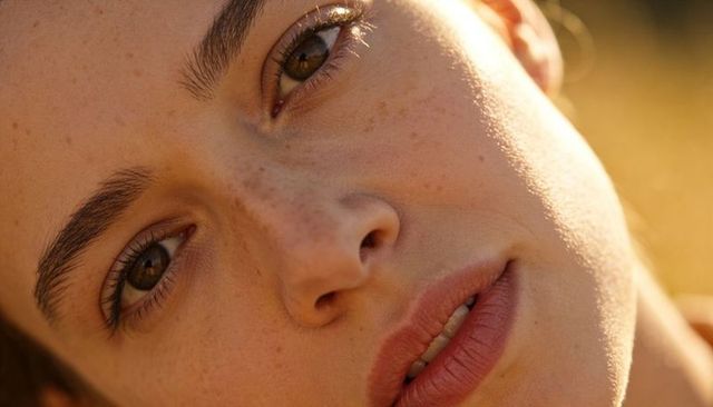 Sunlit closeup of freckled woman gazing with gold eyeshadow and soft natural glow