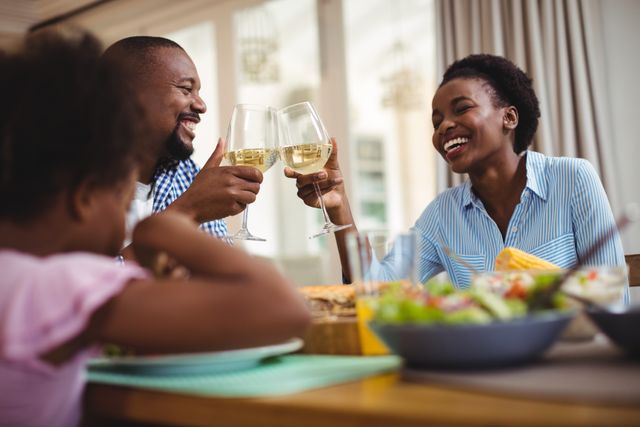 This image depicts a joyful family toasting glasses of wine while enjoying a meal at home. Perfect for use in advertisements, articles, or blogs about family gatherings, celebrations, and home dining experiences. It highlights themes of togetherness, happiness, and bonding.