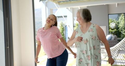 grandmother and granddaughter are captured in a moment of joy as they dance together indoors. smiling widely, they exude a sense of warmth and connection, perfect for illustrating family bonding, intergenerational relationships, or an active and happy lifestyle at home.