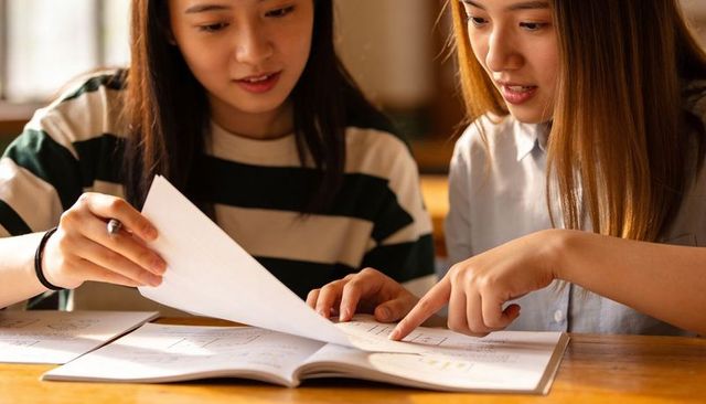 Two women collaborating and studying at cafe table pointing at notebook and diagrams