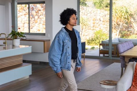 African american man walking through modern open-plan home wearing denim jacket
