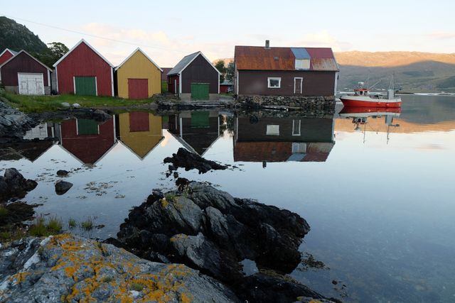 Colorful fishing houses along a calm Norwegian fjord, with perfectly mirrored reflections on water. Perfect for themes of tranquility, nature, Scandinavian destinations, and serene coastal life. Ideal for travel brochures, nature magazines, and image libraries highlighting Norwegian countryside.
