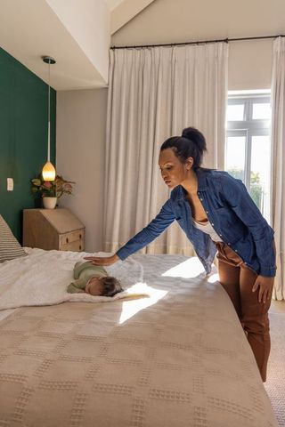 Mother caring for sleeping baby on cozy bed in sunlit bedroom — gentle natural parenting