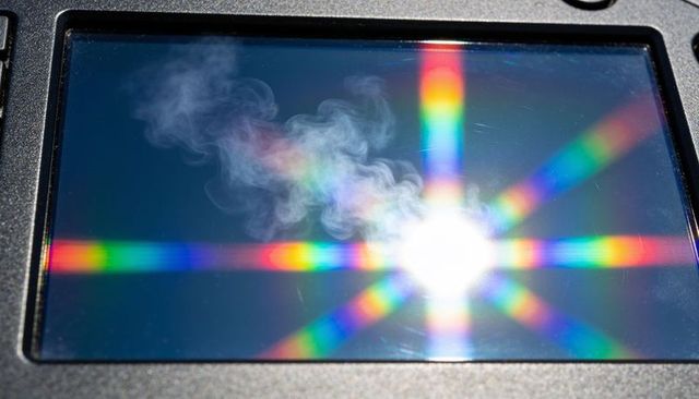 Glossy monitor producing rainbow starburst and diffraction band with smoke wisps on bezel
