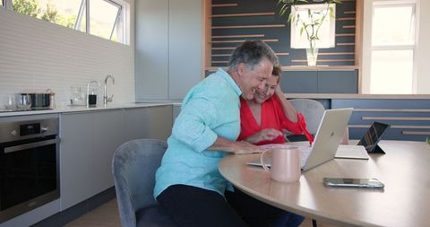 Senior Couple Celebrating Success at Home Using Laptop