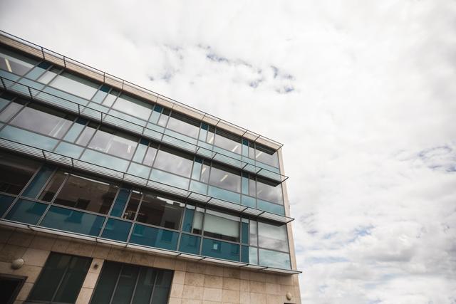 This image showcases the facade of a modern office building with large glass windows against a cloudy sky. Ideal for use in corporate presentations, real estate marketing, architectural portfolios, and business websites to convey a professional and contemporary atmosphere.