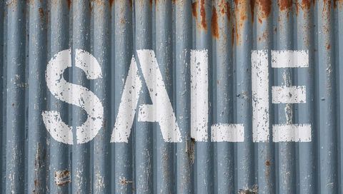 Weathered corrugated metal panel stenciled sale sign with rusty texture and rivets