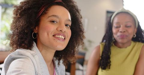 Smiling diverse women leaning toward camera in sunlit cozy living room, casual friendship