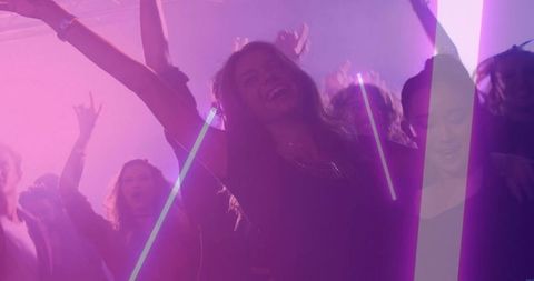 Dancing woman raising arms and smiling in neon nightclub with lasers, haze and lively crowd