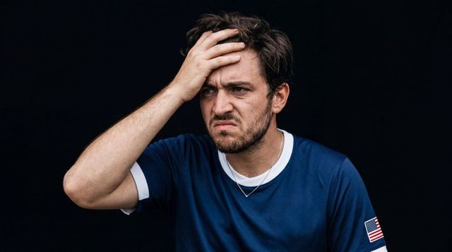 Man holding forehead and furrowing brows, navy shirt with american flag patch