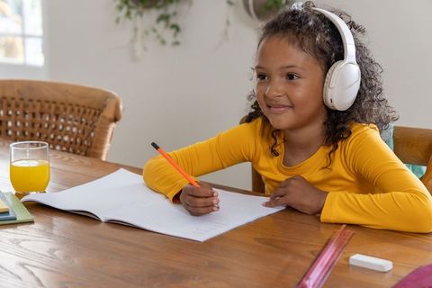 African american girl wearing headphones studying at home writing in notebook