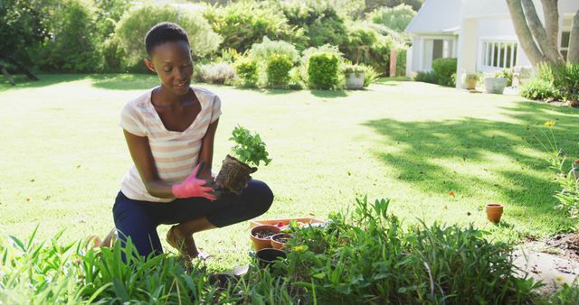 African american woman planting plants in sunny garden smiling to camera. staying at home in isolation during quarantine lockdown.