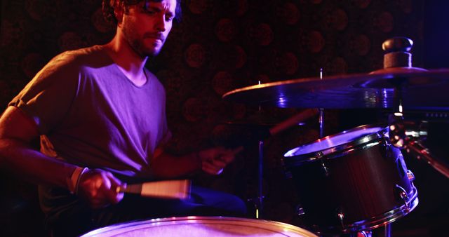 Young man passionately playing a drum set under stage lights. Ideal for use in music-related content, promotional materials for bands and concerts, and articles on live performances and musicianship.