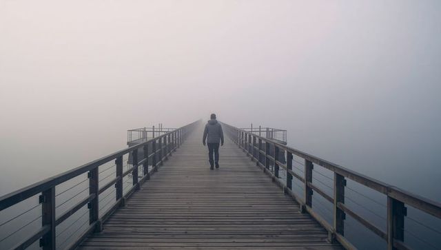 Solitary walker crossing foggy wooden pier into mist - minimalist solitude concept scene